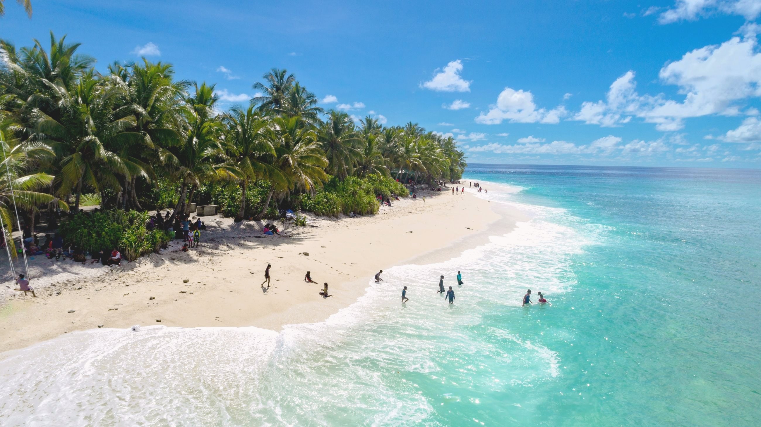 A white sand beach lined with palms beside turquoise water